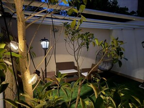 Zona patio con tavolo e sedie, circondata da vegetazione e un muro.