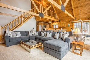 A spacious living room with a large sectional sofa, a coffee table, and a staircase leading to an upper level.