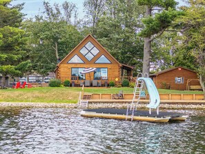 A log cabin with a deck, a floating dock, and a small boat.