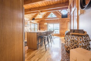A wooden interior with a kitchen island, bar stools, and a woven side table.