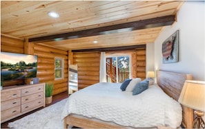 Ein Schlafzimmer in einer Blockhütte mit einem Bett, einem Fernseher, einer Kommode und einem Fenster mit Blick ins Freie.