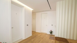 Un couloir avec trois portes blanches, un plancher en bois, un banc marron et une plante en pot.