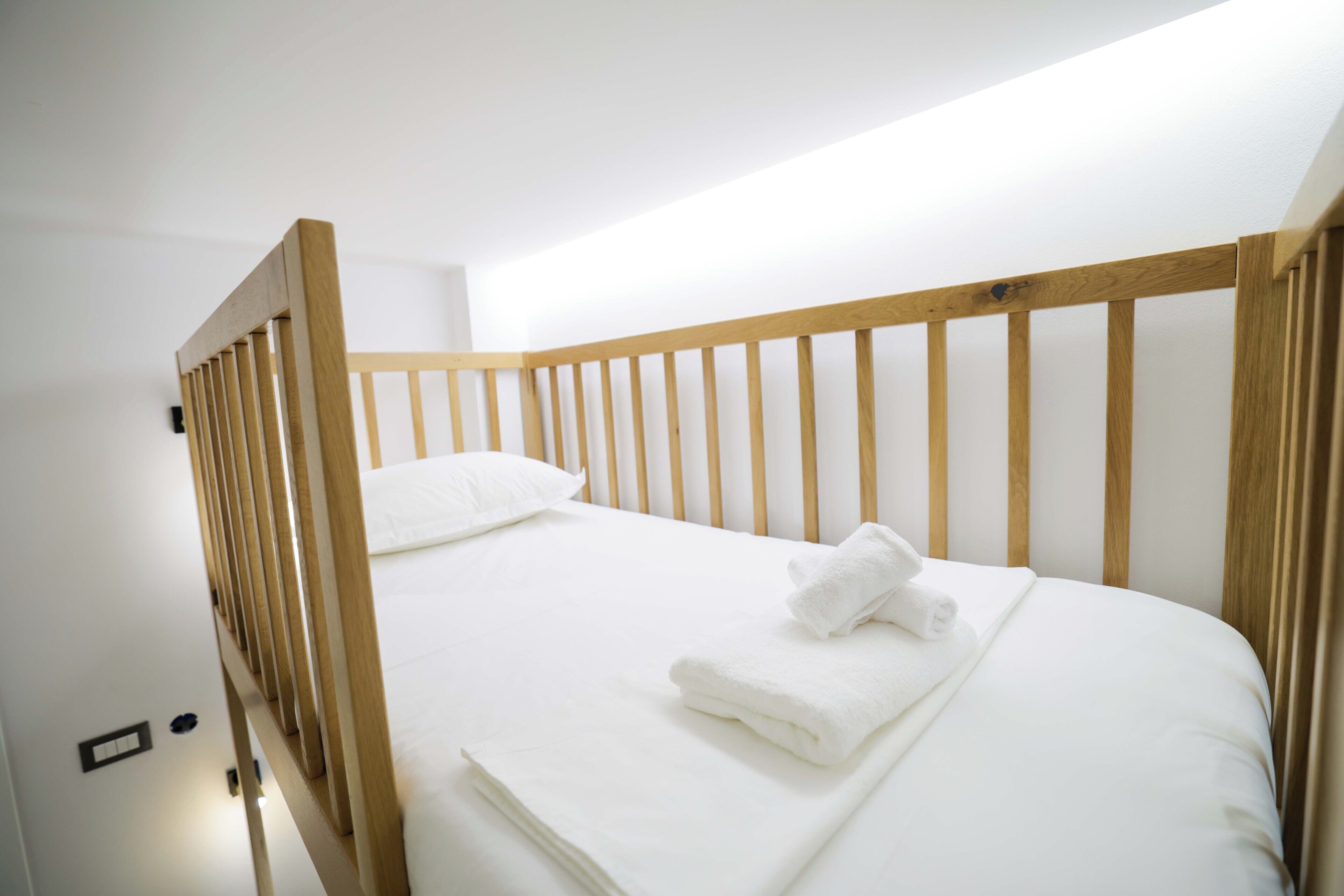A single bed with a wooden frame, white bedding, and a folded white towel.