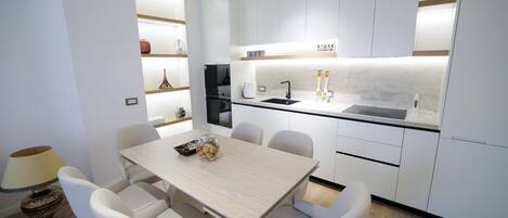A modern kitchen with white cabinetry, a black sink, and a dining table with chairs.