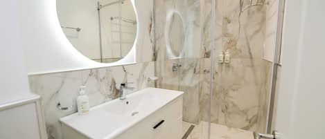 A modern bathroom with a marble vanity, a glass shower enclosure, and a round mirror.