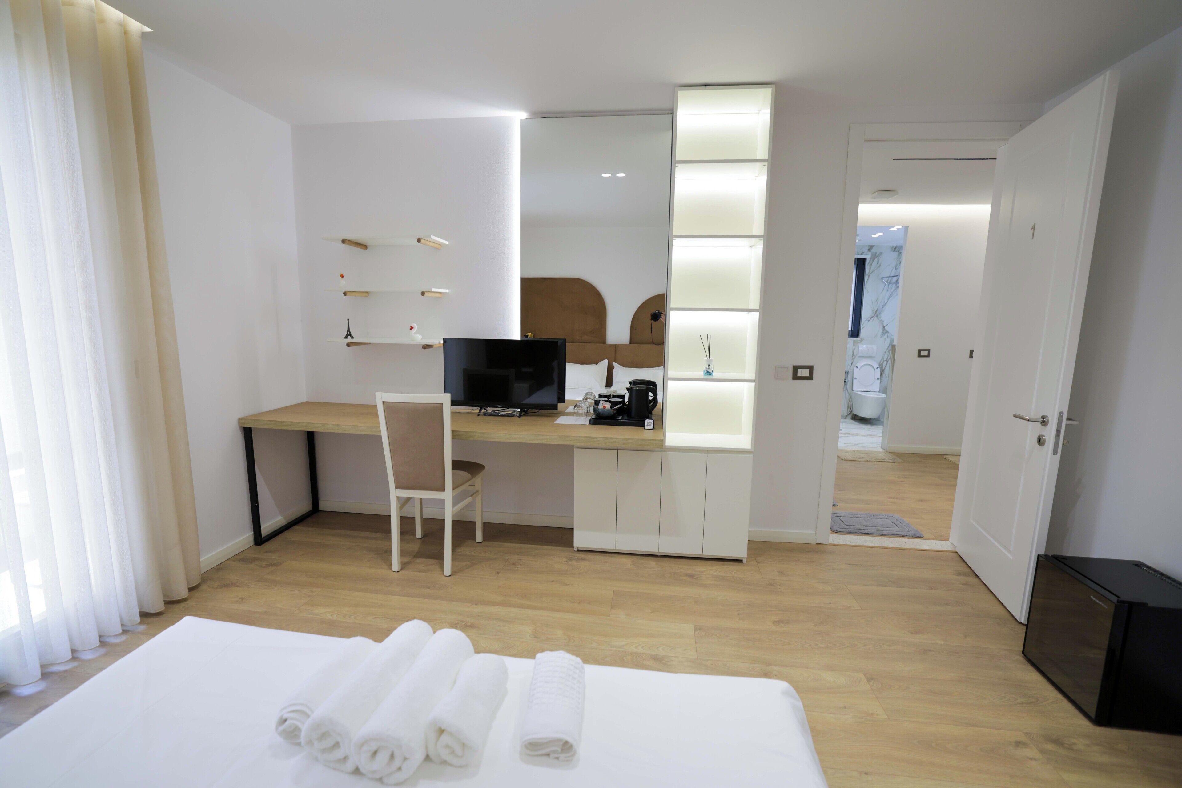 A hotel room with a bed, a desk with a computer, a chair, and a bathroom visible through an open door.