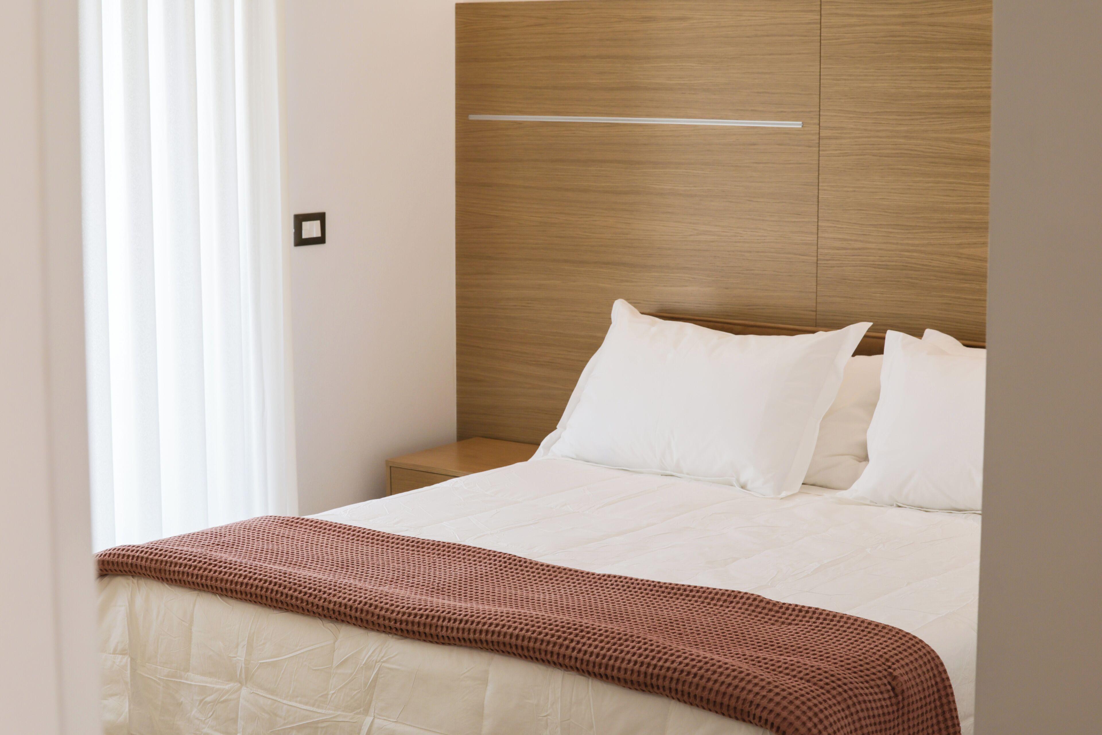A hotel room with a bed, a bedside table, and a window with curtains.