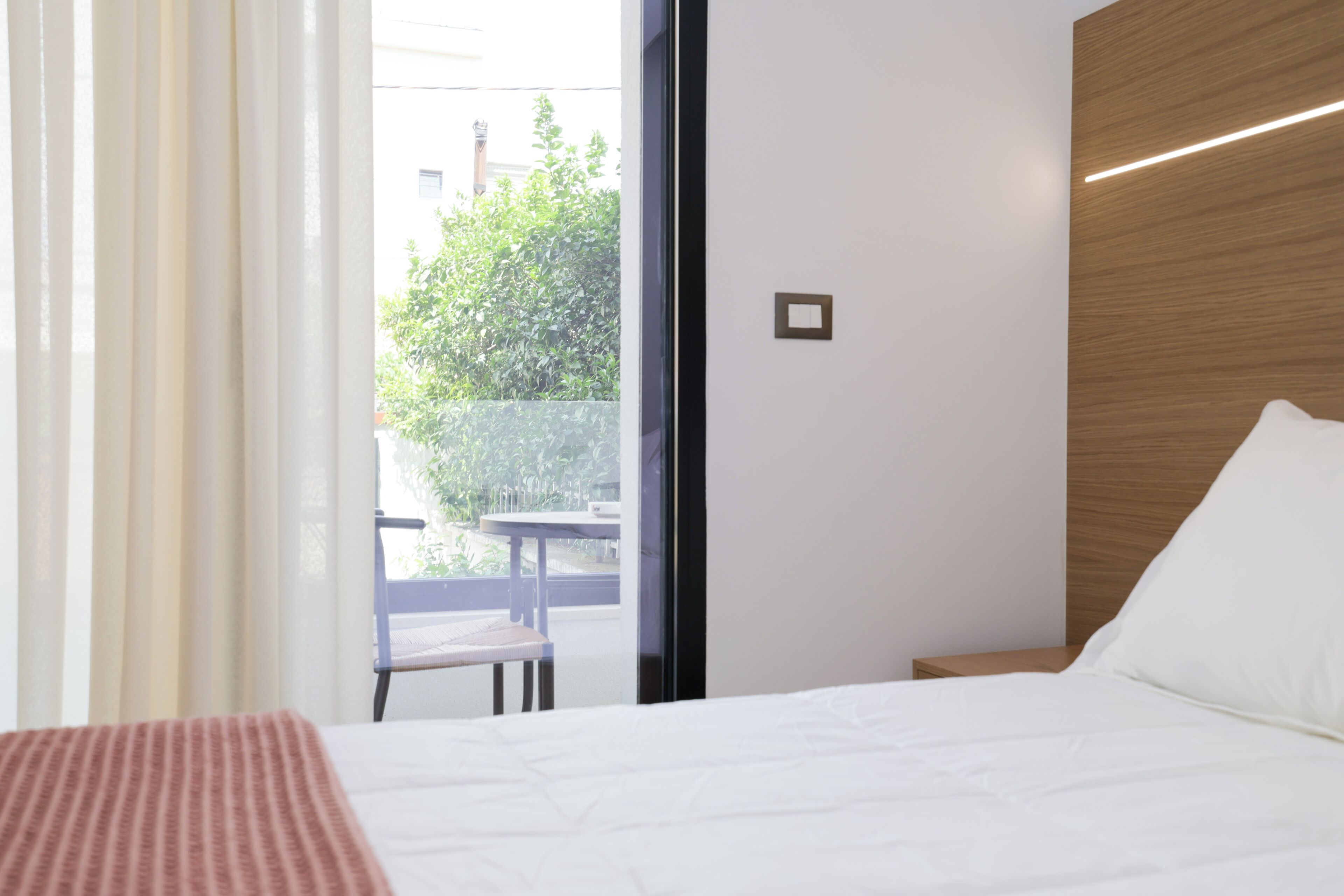 Ein Hotelzimmer mit Bett, einem Fenster mit Vorhängen, einer Holzvertäfelung und einem kleinen Tisch.