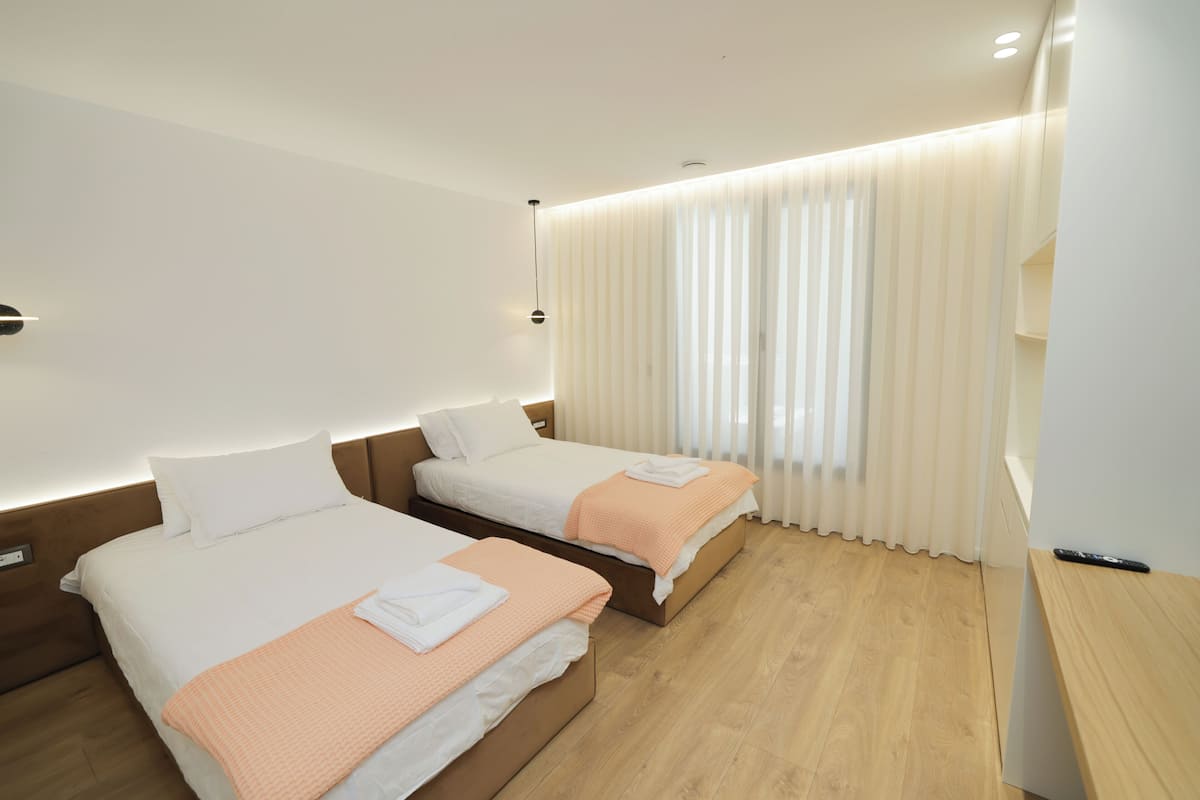 Habitación de hotel con dos camas, piso de madera, mesita de noche y ventana con cortinas.