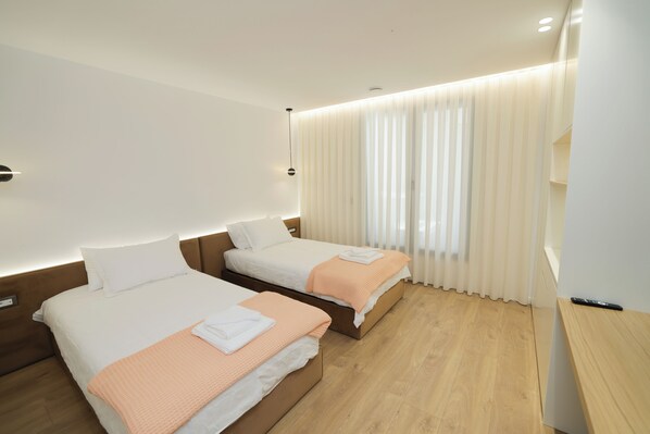 Habitación de hotel con dos camas, piso de madera, mesita de noche y ventana con cortinas.