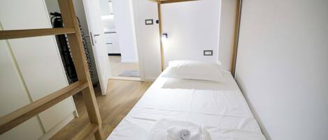 A single-bed room with a wooden frame, white bedding, and a towel on the bed.
