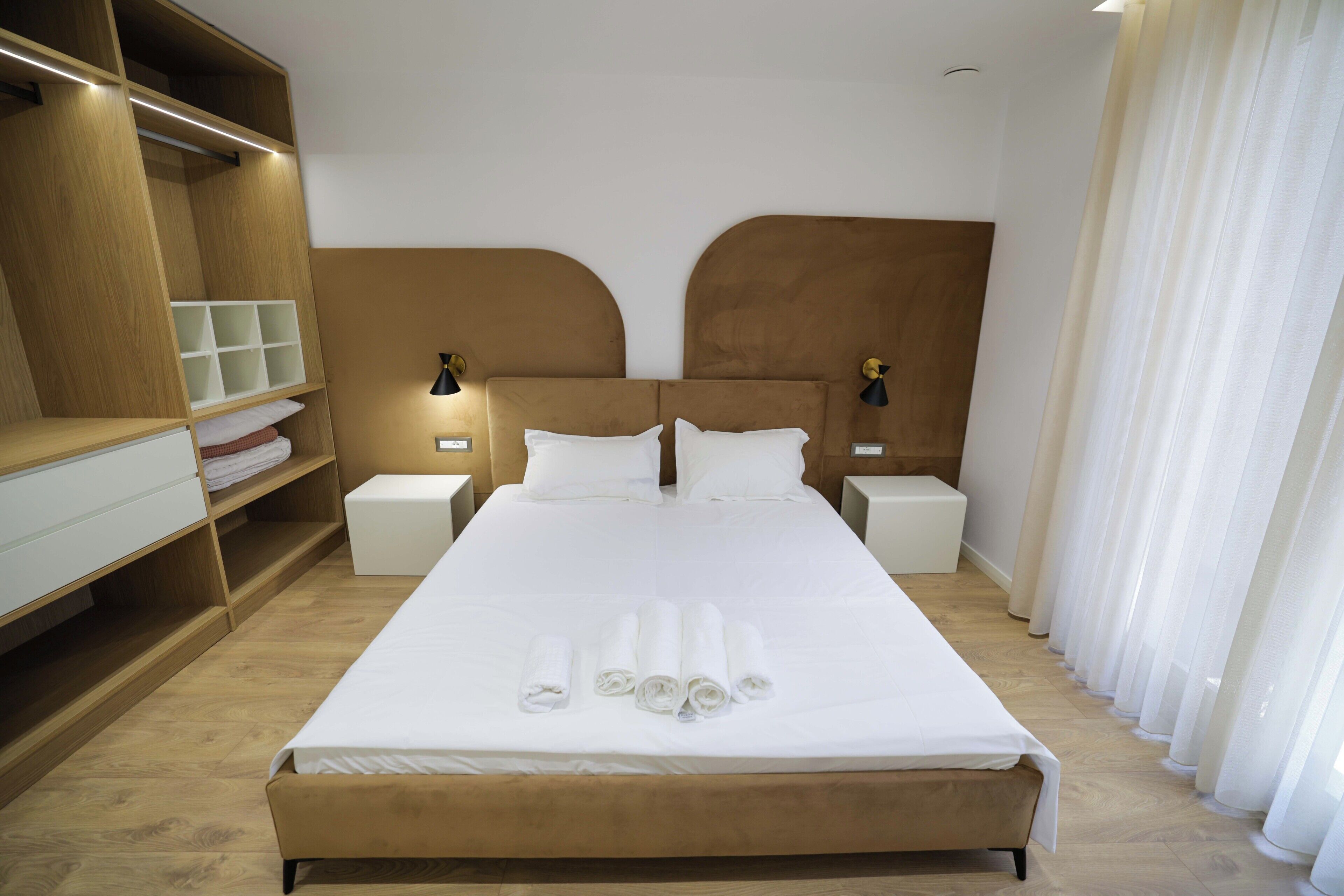 A hotel room with a large bed, two bedside tables, a wardrobe, and a window with curtains.