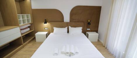 A hotel room with a large bed, two bedside tables, a wardrobe, and a window with curtains.