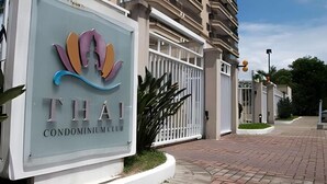 Segnaletica per 'Thai Condominium Club' con un logo moderno, un ingresso recintato e una strada privata asfaltata.