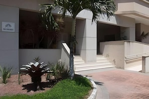 Ein Gebäudeeingang mit einer Palme, Stufen und einem Schild.