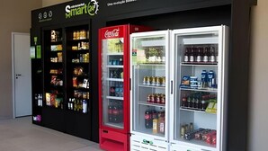 Un'area con distributori automatici, tra cui macchine Coca-Cola, e un cartello Smart+24.