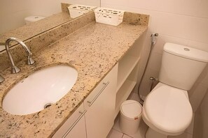 A bathroom with a granite countertop, a white sink, a toilet, and a trash can. - EXECUTIVE IN - IDEAL FOR FAMILIES (Rio de Janeiro)