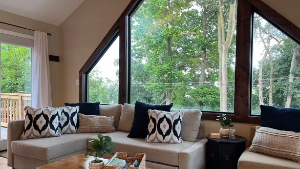 Ein gemütliches Wohnzimmer mit Sofa, Couchtisch und großen Fenstern, die einen Blick auf Bäume bieten.