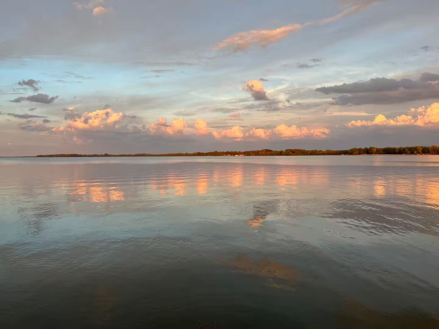 Un lac paisible, avec une rive lointaine, un ciel dégagé et quelques nuages épars.