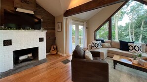 Ein modernes Wohnzimmer mit Kamin, Holzbalken, einer Couch und einem großen Fenster.