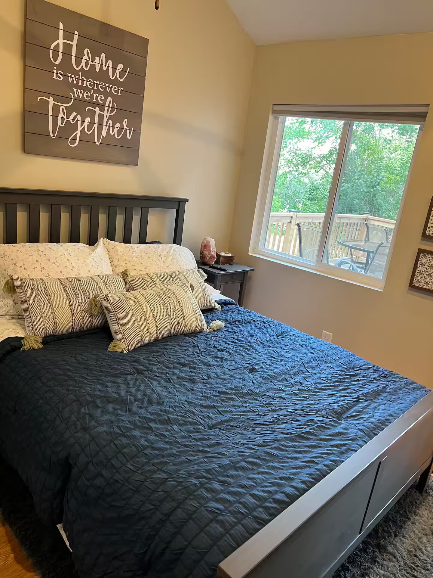A bedroom with a bed, a nightstand, a window, and a wall sign.