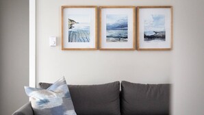 En grå sofa med en pude, tre billeder i rammer på væggen og en termostat.