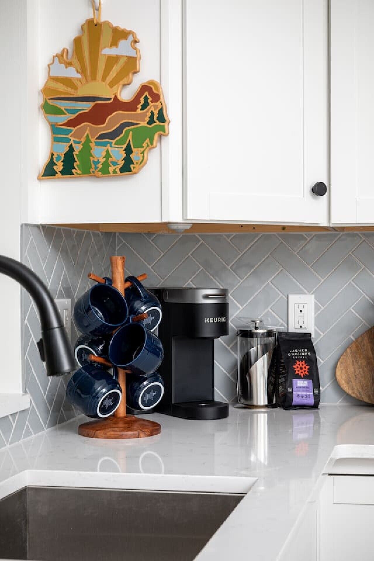 Una cocina con cafetera, un soporte para tazas y un adorno en la pared.