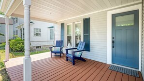 Eine überdachte Veranda mit zwei Adirondack-Stühlen, einer blauen Tür und einer weißen Außenwand.