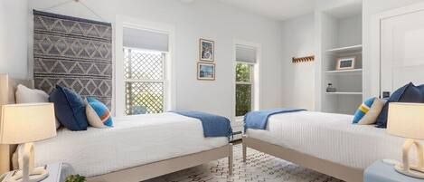 A bedroom with two beds, a desk, a chair, a lamp, a plant, and a patterned rug.