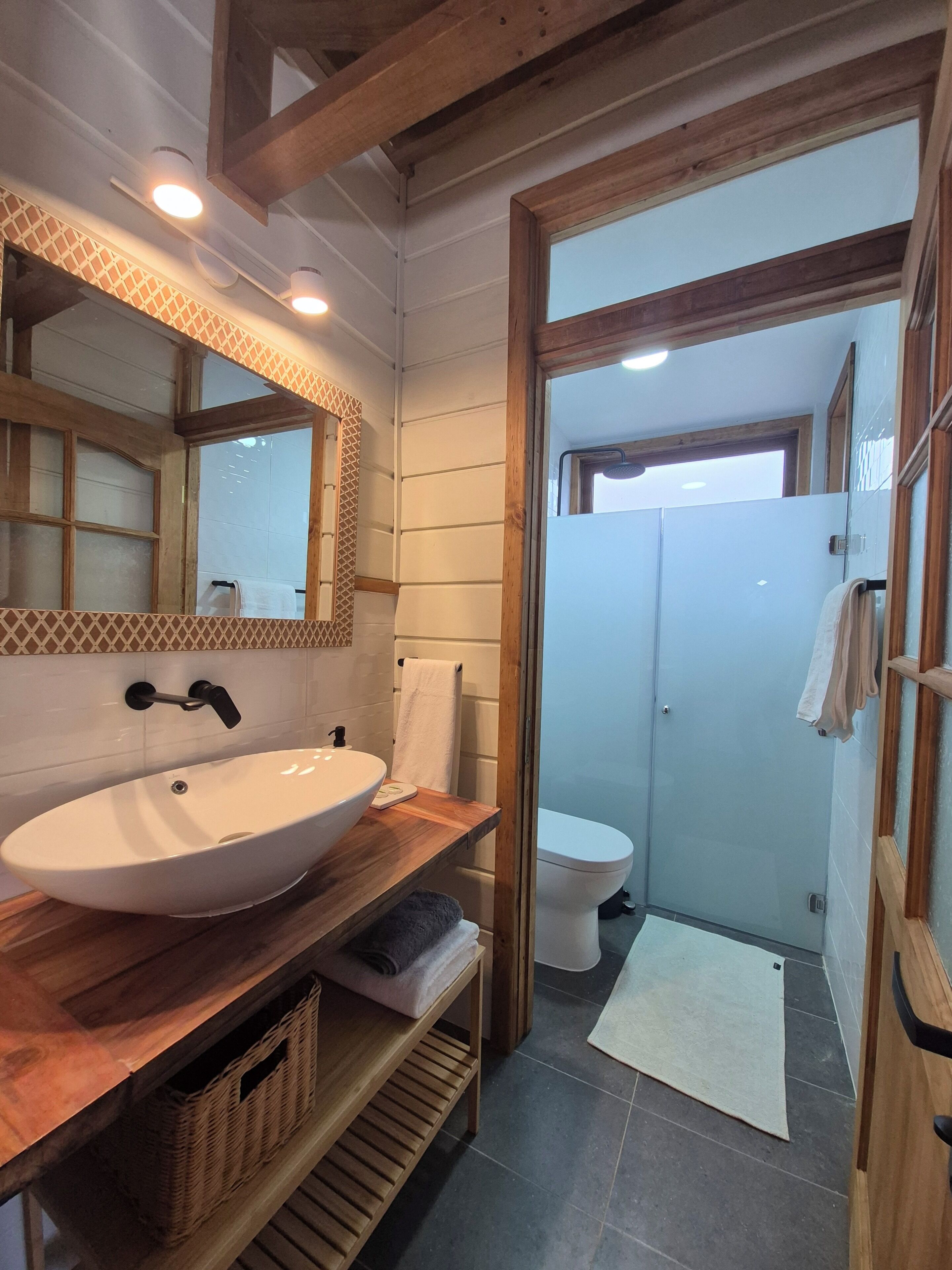 A bathroom with a wooden vanity, a large mirror, a white sink, and a shower area.