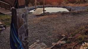 A wooden deck with a stone pillar, a wooden bridge, and a view of the sunset over water. - La Vertiente Pullay (Cobquecura)