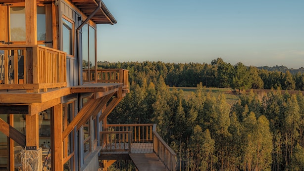 A wooden multi-story building with large windows and a deck, surrounded by a forested landscape. - La Vertiente Pullay (Cobquecura)