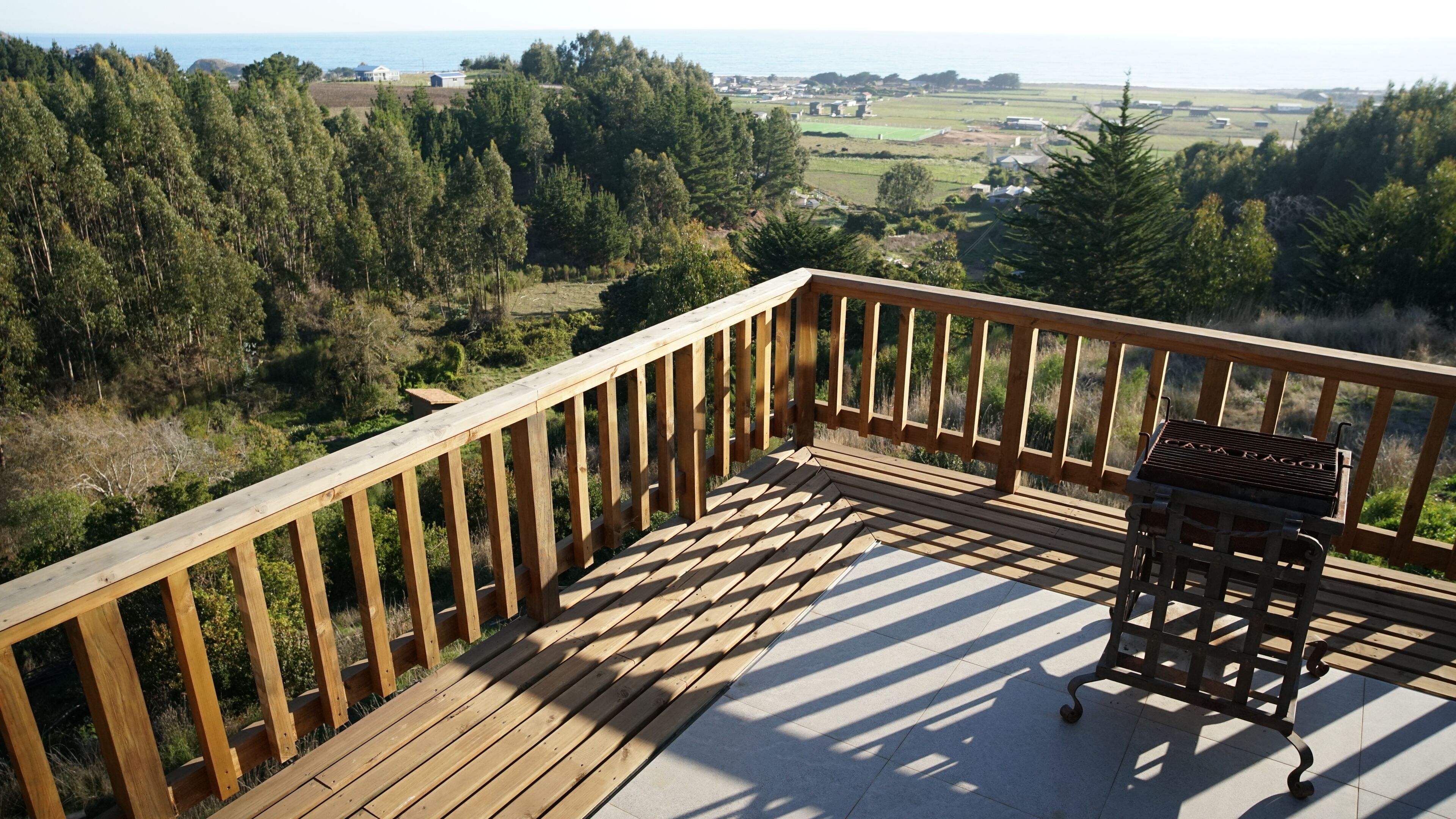 Una terraza de madera con una parrilla y vistas a un paisaje boscoso.