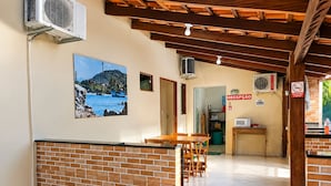 A reception area with a reception desk, a sign indicating 'Reception,' and a no-smoking sign. There are air conditioning units mounted on the wall, a framed picture of a coastal scene, and a tiled floor.