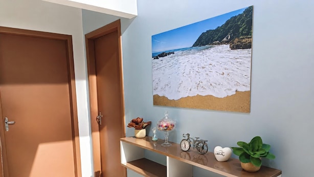 A hallway with a wooden door, a small shelf with decorative items, and a beach-themed wall art.