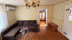 A room with a sectional sofa, a small round table with a vase of flowers, a wooden cabinet, and a door with a number. - Historic Summer cottage in Jurmala (Jūrmala)