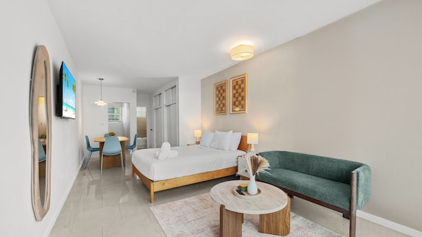 Ett modernt hotellrum med en säng, en soffa, ett matbord med stolar, en TV och en spegel.