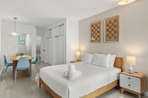 A hotel room with a bed, bedside tables, a desk with chairs, and artwork on the wall. - Charming studio apartment in delightful Miami Beach with cool AC (Miami Beach)