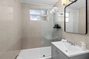 A modern bathroom with a glass shower enclosure, a bathtub, a vanity with a sink, and a large mirror. - Charming studio apartment in delightful Miami Beach with cool AC (Miami Beach)
