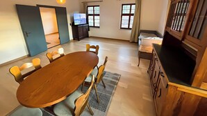 Una habitación con una mesa de comedor de madera, sillas, un televisor, una cama y una ventana con cortinas.
