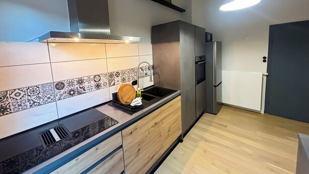 Una cocina moderna con encimera negra, armarios de madera, campana extractora de acero inoxidable y horno empotrado.