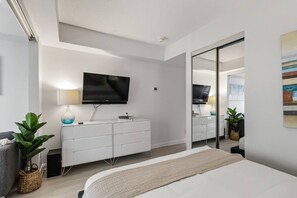 A modern bedroom with a bed, a TV, a dresser, and a mirror.