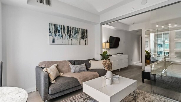 Ein modernes Wohnzimmer mit grauem Sofa, einem weißen Couchtisch und einem großen, abstrakten Gemälde an der Wand.