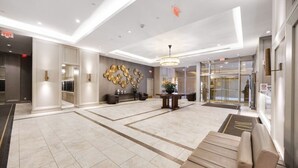 Eine geräumige Lobby mit Marmorboden, einer Rezeption, einer Wanduhr und einer Treppe zu einer oberen Ebene.