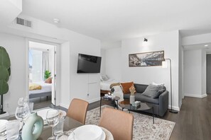 Ein modernes Wohnzimmer mit einer Couch, einem Couchtisch, einem Flachbildfernseher und einem Essbereich mit Stühlen und einem Tisch für zwei Personen.