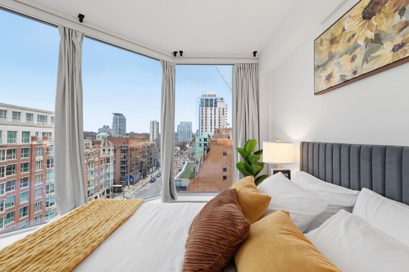 Ein Hotelzimmer mit großem Fenster, einem Bett mit weißer Bettwäsche, einem grauen Polsterkopfteil und einem Bild an der Wand.