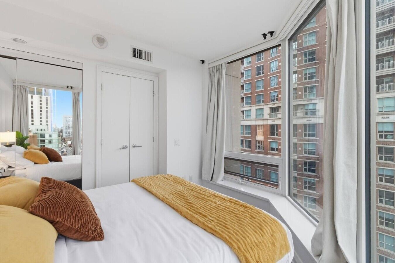 Een hotelkamer met een bed, een groot raam, een kledingkast en uitzicht op een stadsgezicht.