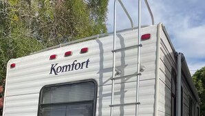 Valkoinen matkailuauto, jonka kyljessä näkyy merkki ’Komfort’, siinä on takaikkuna ja tikkaat.