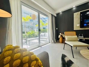 A modern hotel room with a large sliding glass door to a balcony, a flat-screen TV mounted on the wall, and a comfortable seating area with a sofa and a chair. - 2-bedroom apartment in fantastic Punta Cana with AC and gym (Punta Cana)