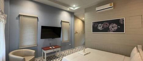 Un dormitorio con cama, televisor, sillón, una mesita y equipo de aire acondicionado.